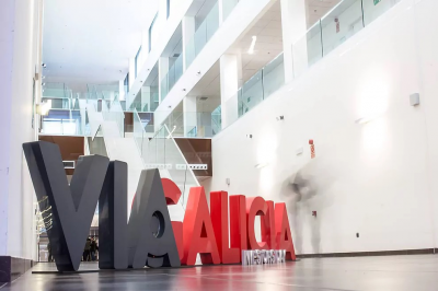 A ViGalicia sign is shown, with its logo and name, while the headquarters or office can be seen in the background, highlighting the institutional environment of the entity.